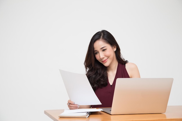 Photo young asian woman reading document paper and sitting with computer laptop on wood table