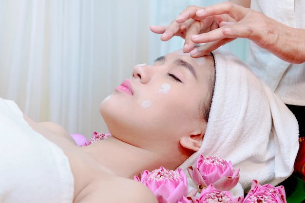 Young Asian woman receiving clay facial mask in spa beauty salon