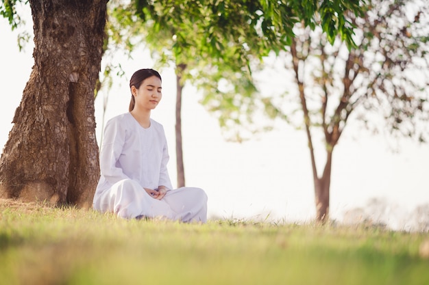 Foto la giovane donna asiatica si distende la meditazione bianca d'uso del vestito ai campi di erba verde