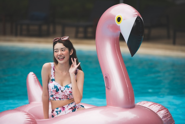 Young Asian woman ride on Giant Inflatable Swan in swimming pool.