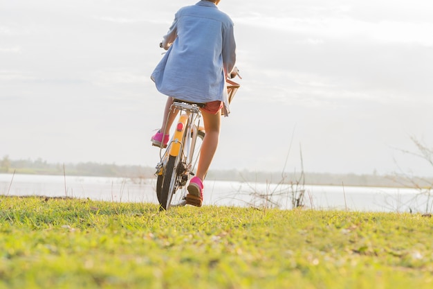Giovane bicicletta asiatica di guida della donna al parco con il tramonto