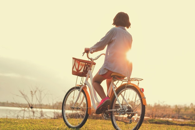 Молодая азиатская женщина, езда на велосипеде в парке с закатом