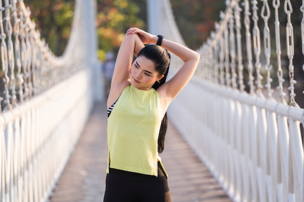 A young Asian woman runner athlete in sports outfit doing stretching and warm up before workout, jogging and fitness training session in the city park in the morning. Sports and recreation