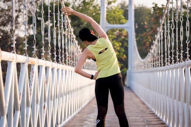 A young Asian woman runner athlete in sports outfit doing stretching and warm up before workout, jogging and fitness training session in the city park in the morning. Sports and recreation