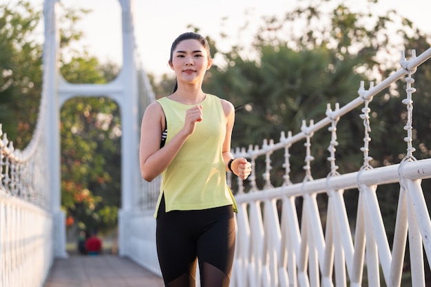 Una giovane atleta asiatica del corridore in abbigliamento sportivo che fa jogging e si allena nel parco della città al mattino. stile di vita sano giovane donna asiatica sportiva in esecuzione al parco tropicale. sport e ricreazione