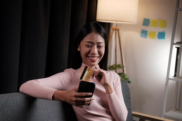 Young Asian woman shopping online via credit card while sitting on sofa at home