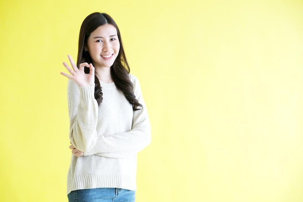 Young asian woman showing ok hand sign while standing over isolated yellow background