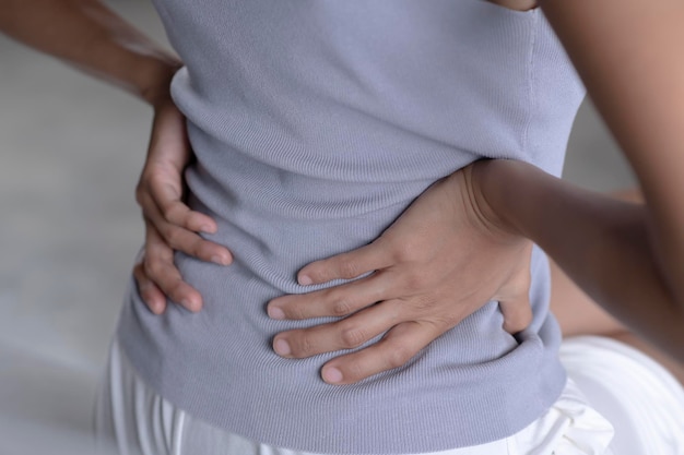 Young Asian woman sitting on bed and suffering from back pain Adult female is holding her lower back and suffering from chronic back pain Health care and medical concept