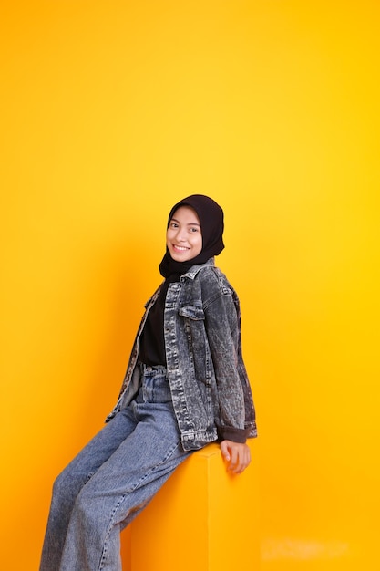 young asian woman sitting and laughing on a yellow background