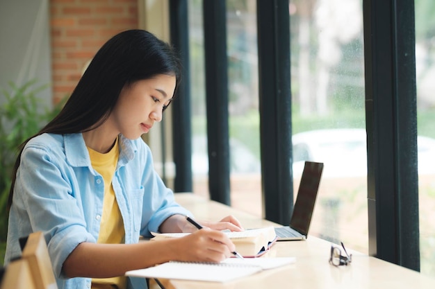 Young asian woman sitting at table and writing on notebook