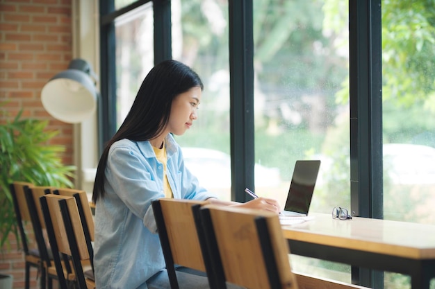 테이블에 앉아서 노트북에 글을 쓰는 젊은 아시아 여성