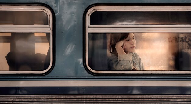 Photo young asian woman sitting in train and looking through the window