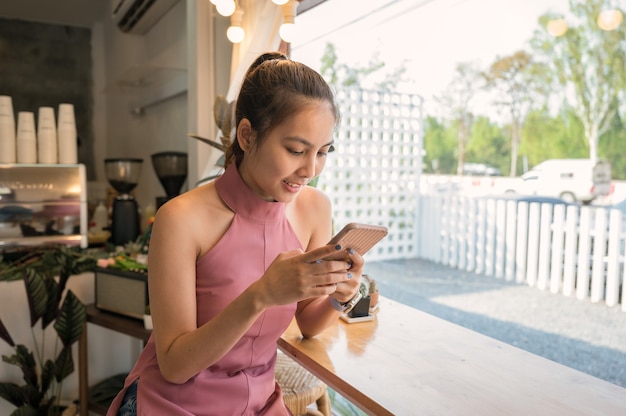 Giovane donna asiatica seduta e utilizza lo smartphone sul bancone vicino alla finestra nella caffetteria