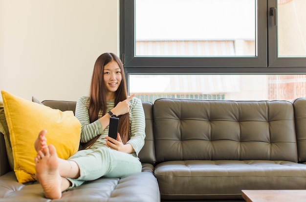 Young asian woman smiling cheerfully, feeling happy and pointing to the side and upwards, showing object in copy space