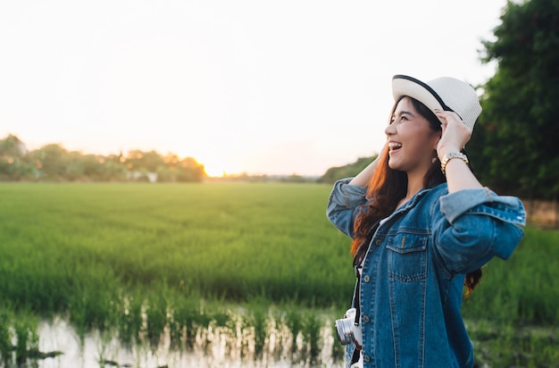 アジアの若い女性が帽子に笑みを浮かべてします。夕日と美しい自然を楽しんでいる女の子。