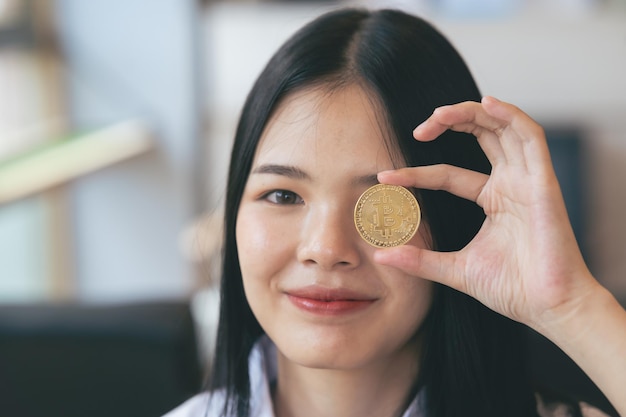 La giovane donna asiatica sorridente tiene la criptovaluta bitcoin a casa