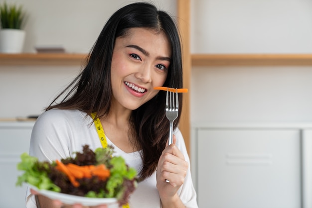 Young asian woman smiling lose weight eating vegetable salad in dishes on her hand, Dieting and good health concept