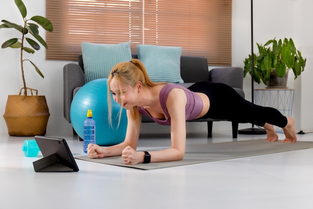 Young Asian woman in sportswear doing plank exercise and watching fitness tutorial online video on tablet