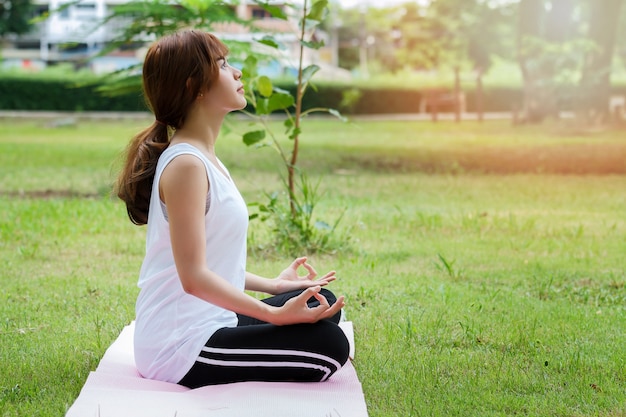 Giovane donna asiatica in abiti sportivi che meditating mentre sedendosi nella posa del loto sulla stuoia di yoga