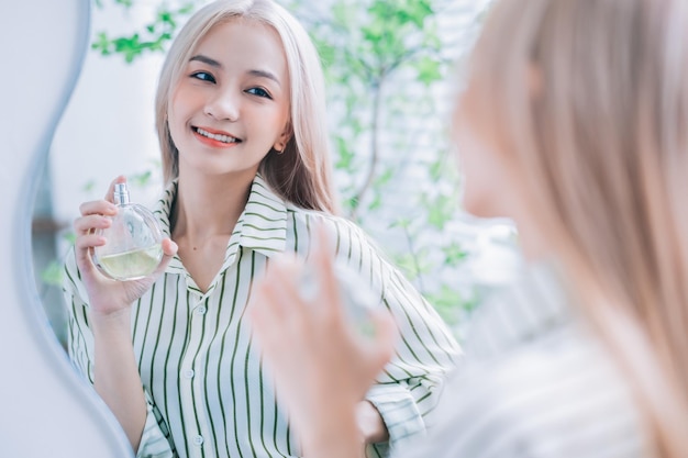 거울 앞에서 향수를 뿌리는 젊은 아시아 여성