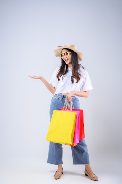 Giovane donna asiatica stare in possesso di una borsa della spesa multicolore e stese la mano con una faccia felice su sfondo bianco.