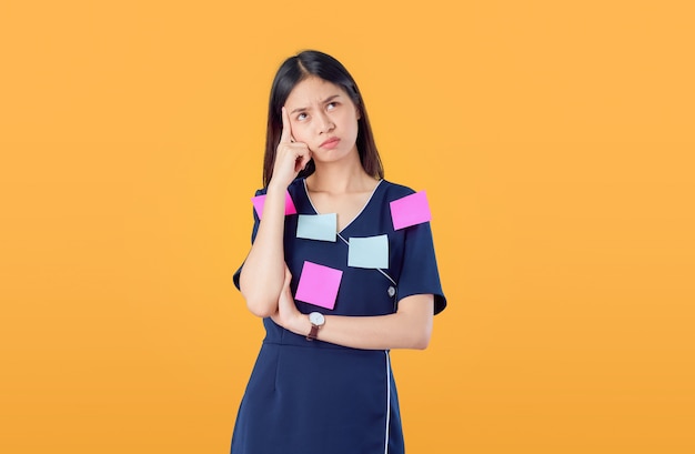 Young Asian woman standing pointing finger and think something with crossed arms against, post notes on the body