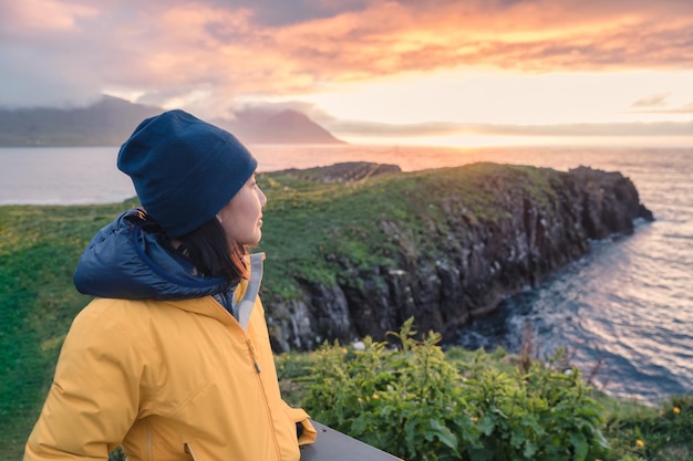 Young asian woman standing and watching puffin bird on the cliff among arctic ocean in Borgarfjordur Eystri on summer at East of Iceland