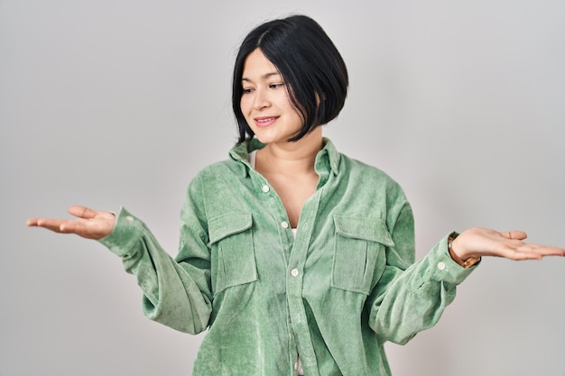 Young asian woman standing over white background smiling showing both hands open palms, presenting and advertising comparison and balance