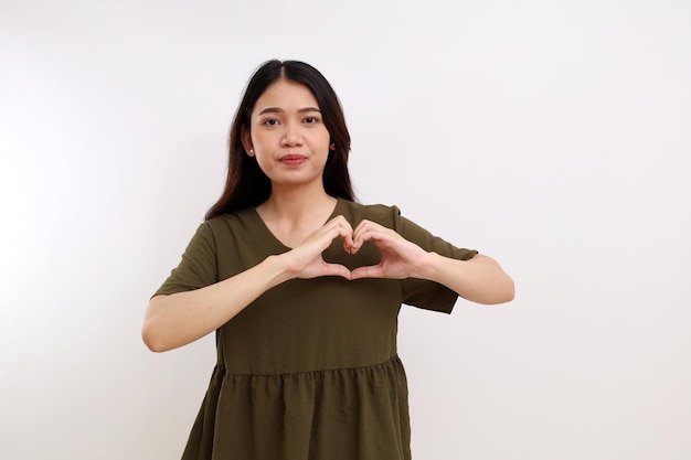 Young asian woman standing with love shape hand on her chest\
heart health concept isolated on white