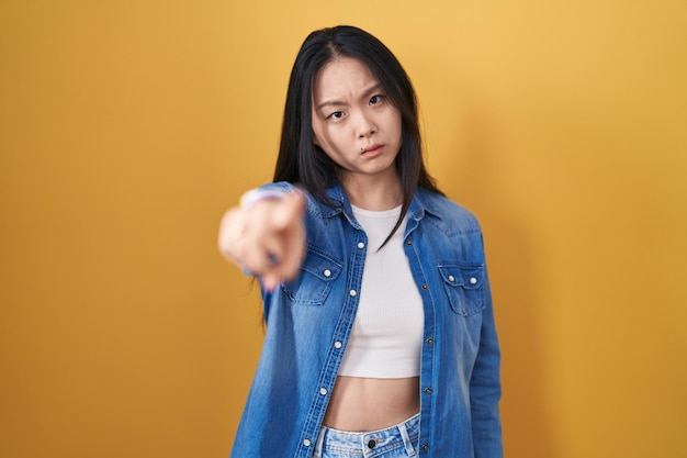 Young asian woman standing over yellow background pointing displeased and frustrated to the camera angry and furious with you