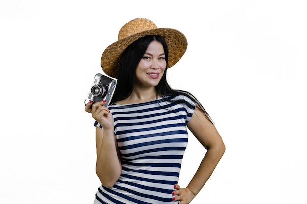 Молодая азиатка в соломенной шляпе позирует с винтажной фотокамерой, изолированной на белом