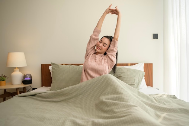 young asian woman stretching in bed after waking up in the morning