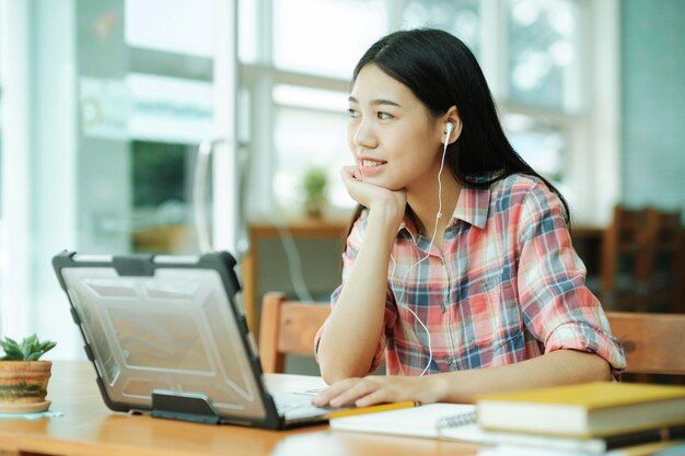 Photo young asian woman study in front of the laptop computer and and using headphones at offsitexa