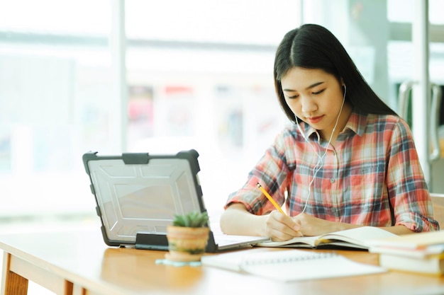 La giovane donna asiatica studia davanti al computer portatile e usa le cuffie su offsitexa