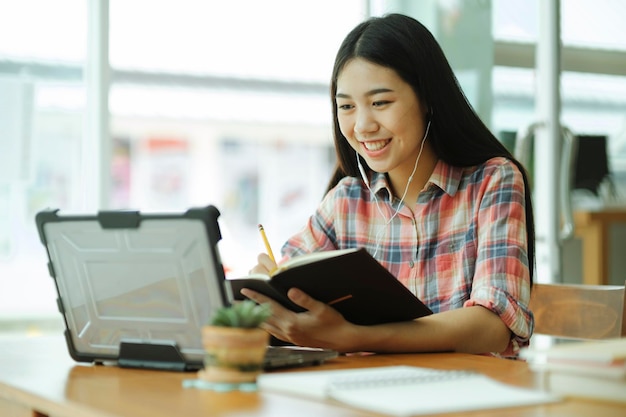 La giovane donna asiatica studia davanti al computer portatile e usa le cuffie su offsitexa