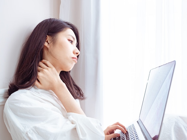 Young asian woman suffering from pain in shoulder when using laptop