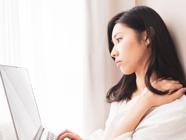 Young asian woman suffering from pain in shoulder when using laptop