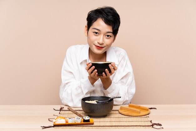 Young Asian woman in a table with bowl of noodles and sushi