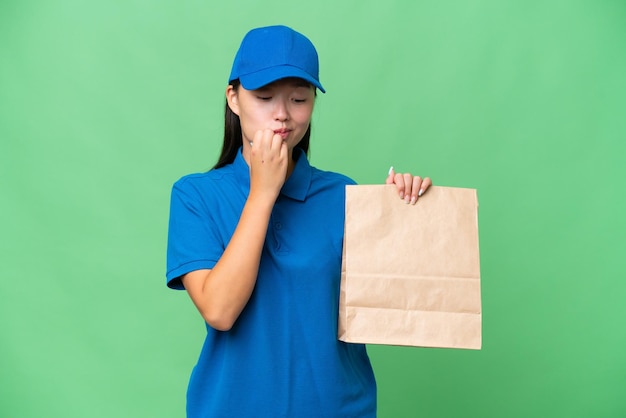 Young Asian woman taking a bag of takeaway food over isolated background having doubts