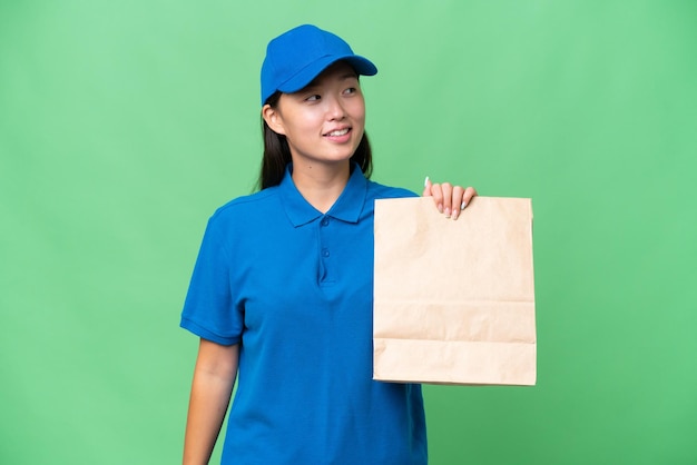 Young Asian woman taking a bag of takeaway food over isolated background looking to the side and smiling