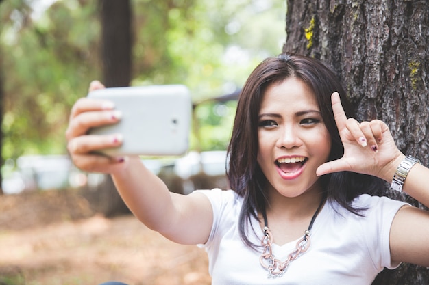 Giovane donna asiatica che prende un selfie mentre sedendosi all'aperto