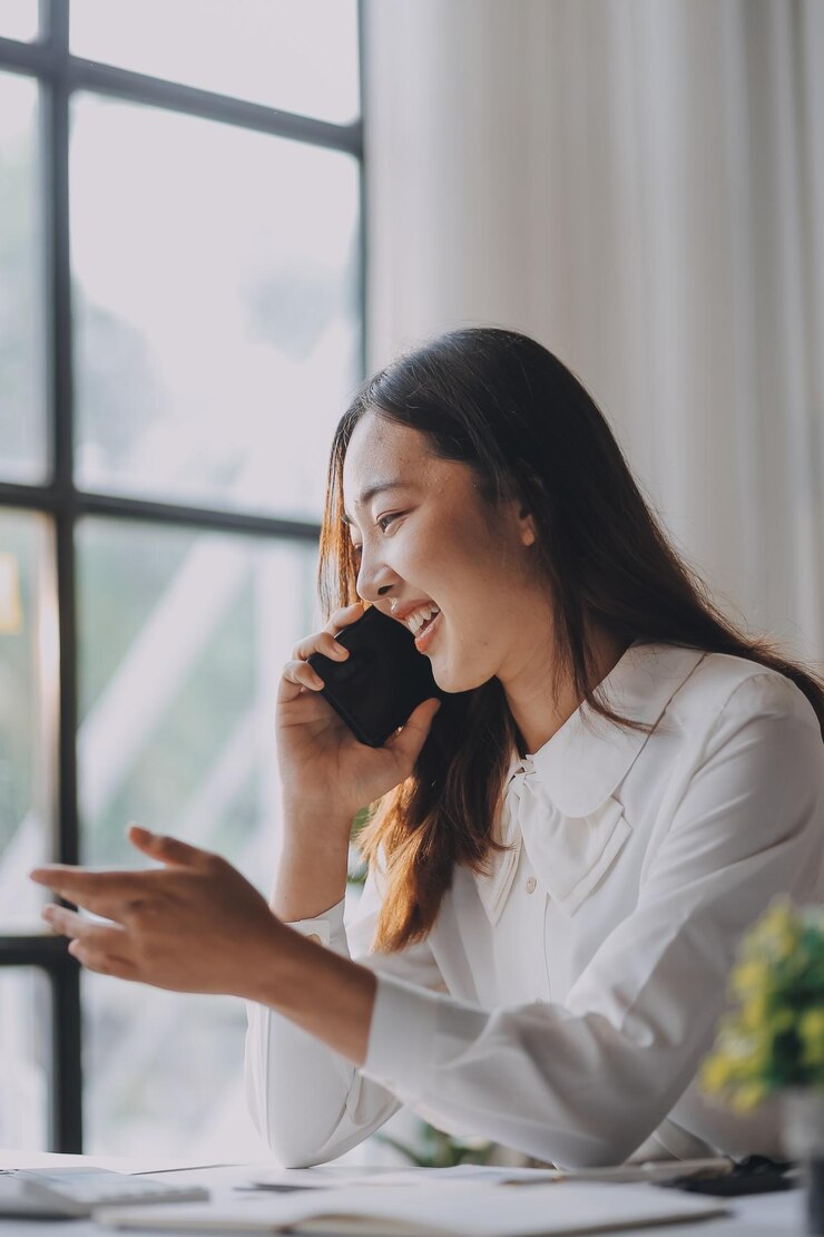 Photo アジアの女性が携帯電話で話しながらメモをとりながら自宅でラップトップコンピュータで仕事をしていますビジネスホームオフィスとテクノロジーコンセプト
