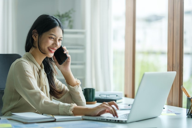 Young asian woman talking on mobile phone and working online with laptop computer at outdoor