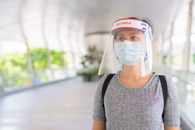 Young Asian woman thinking with mask and face shield for protection from corona virus outbreak in the city