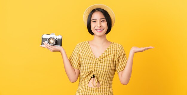 Turista della giovane donna asiatica che tiene macchina fotografica e che osserva su sfondo arancione.