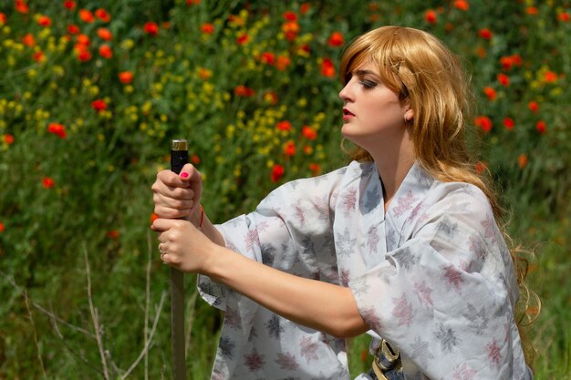 Young asian woman in traditional kimono trains fighting techniques with katana sword on the hills with red poppies, samurai warrior girl