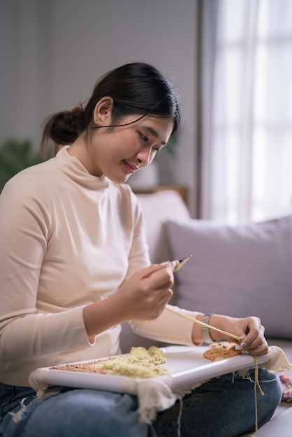 Foto giovane donna asiatica usa ago e filato per ricamare artigianato su telaio in stile di vita hobby