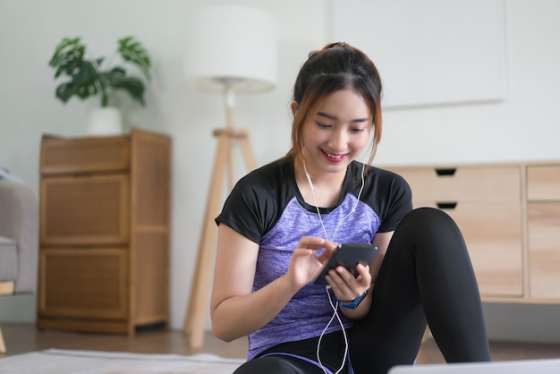 Young asian woman use smartphone surfing internet and listening music after doing exercise at home