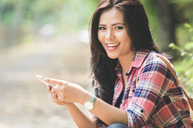 Young asian woman using a cellphone while sitting on the park