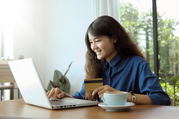 Young asian woman using computer with a credit card to shopping online in coffee shop. 